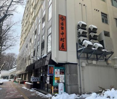 Snow-covered sidewalk and multi-story ryokan facade with vertical sign reading Nakamuraya Ryokan in Hokkaidō
