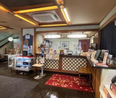 Warm ryokan reception with wooden counter, souvenir display case, brochure stand and polished floors at Nakamuraya Ryokan in Hokkaidō
