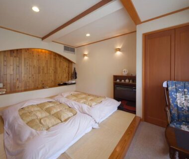 Tatami room with two futon mattresses, wooden accent wall and folded robe on chair at Nakaodaira, Gifu