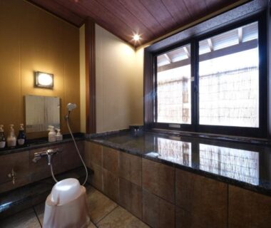 Tiled Japanese bathing area with stool, handheld shower and large window at Nakaya Ryokan, Gunma