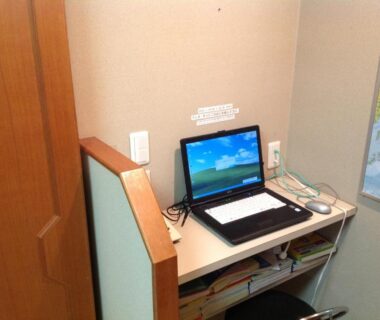 Compact ryokan room desk with open laptop, shelving under desk and wall map at Nakayasu Ryokan Ishikawa