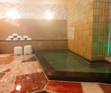 Indoor tiled onsen bath with low washing stools and stacked basins at Nakayasu Ryokan, Ishikawa