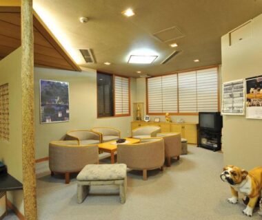 Carpeted guest lounge with armchairs, low tables, shoji screens and decorative wooden dog in Nakayasu Ryokan, Ishikawa