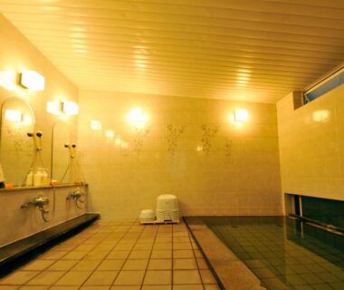 Tiled indoor onsen with wall-mounted shower stations and low stools at Nakayasu Ryokan in Ishikawa, Chūbu