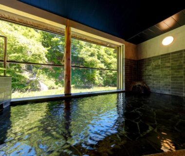 Indoor stone onsen bath with large window overlooking green forest at Namari Onsen Kokoro No Toki, Iwate