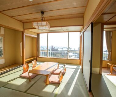 Sunlit tatami room with low table, floor chairs, shoji screens and balcony view at Nangoku Hotel, Chiba