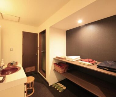Dressing area with two sinks, shelving, slippers and bench at Nanpeidai Onsen Hotel, Tochigi
