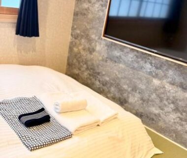 Low bed on tatami with folded towels and yukata, shoji window and wall-mounted TV in Nara Ryokan room