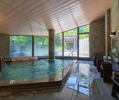 Spacious indoor onsen bath with tiled pool, wooden wash stations and garden view at Narashino no sato Gyokusui Shizuoka