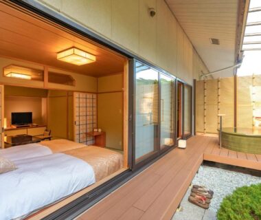Interior tatami room with western bed, shoji screens, deck and outdoor wooden tub at Narashino no sato Gyokusui, Shizuoka