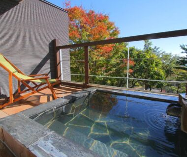 Stone onsen bath on wooden terrace with deck chair and autumn foliage at Nasu Hoshi no Akari, Tochigi