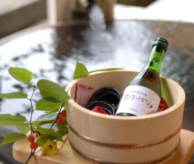 Wooden bucket with chilled bottle and glass on a small stool beside an indoor onsen bath