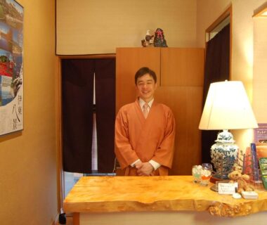 Smiling staff in traditional attire behind wooden reception counter at Nasubi no Hana Shizuoka