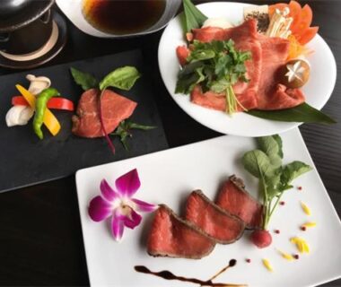 Thinly sliced beef garnished with edible orchid, served with assorted appetizers on dark tableware