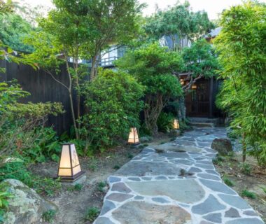 Stone pathway with lanterns leading through a lush garden to a wooden ryokan entrance in Wakayama
