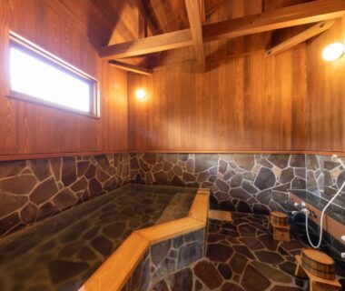 Stone-lined indoor onsen with wooden walls and shower area at Natural Hot Spring Inn Choseian, Wakayama