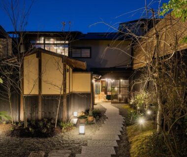 Stone path lit by lanterns leading to Nazuna Kyoto Gosho entrance with garden plants at dusk
