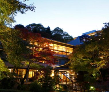 Warmly lit ryokan exterior at dusk with surrounding trees and stone steps in Hyōgo, Kansai