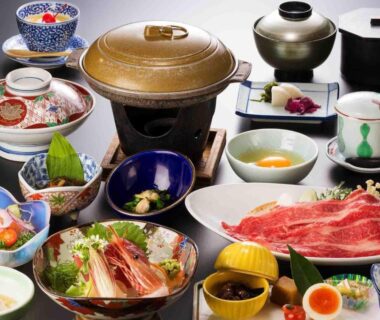 Assorted ryokan dinner bowls with hot pot, thinly sliced beef and side dishes on lacquered table