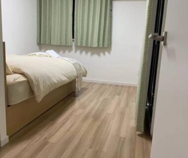 Single bed room with wood flooring, green curtains and air conditioner at New Open Rosenheim ryokan in Tokyo