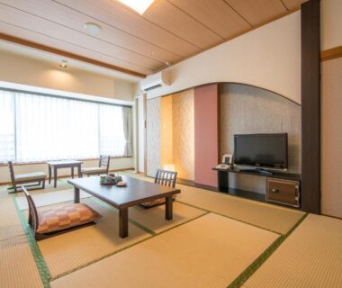 Spacious tatami room with low table, cushions, TV and large window at New Welcity Yugawara, Shizuoka