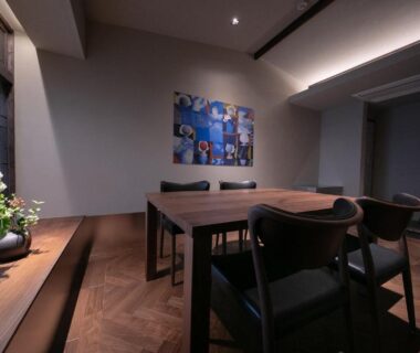 Interior dining area with wooden table, chairs, artwork and floral arrangement at ryokan Nihon-no-Ashitaba in Ōita