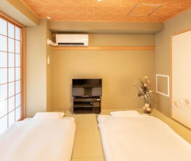 Traditional tatami room with two futons, shoji screens, sliding fusuma doors, small TV and floral arrangement in Tokyo ryokan