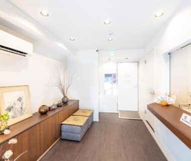 Minimal ryokan reception with wooden counter, bench seating, framed art and glass entrance at Nihonbashi Kakigara Ryokan in Tokyo