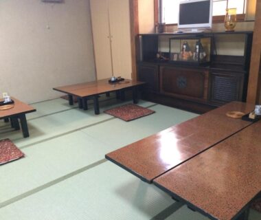 Tatami room with low tables, floor cushions and wooden cabinet at Nihonkan Kyoto