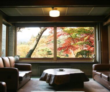 Cozy lounge with sofas and low table overlooking red and yellow maple trees through large window at Nikko Kanaya Hotel