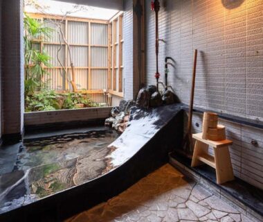 Stone and wooden onsen bath beside a small courtyard garden at Nisainoyuyado Asahiya
