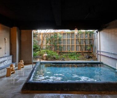 Indoor tiled communal onsen with wooden stools and small garden view at Nisainoyuyado Asahiya in Ōita, Kyūshū