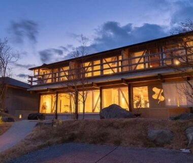 Evening exterior of two-story wooden ryokan with warm interior lighting, Nisainoyuyado Asahiya, Ōita, Kyūshū