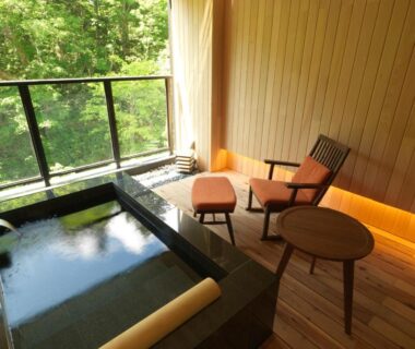 Wooden interior with stone onsen tub and balcony overlooking forest at Niseko Konbu Onsen Tsuruga, Hokkaidō