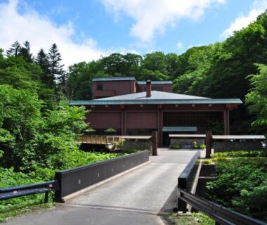 Bridge leading to wooden ryokan building surrounded by lush forest at Niseko Konbu Onsen Tsuruga Moku-no-sho Hokkaidō