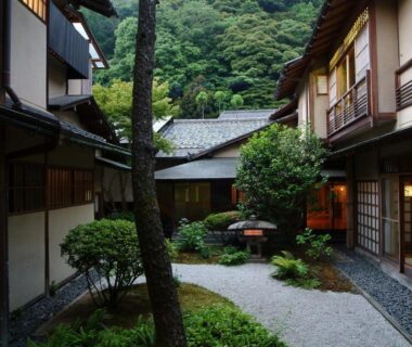 Inner courtyard with gravel path, shoji-screen rooms, manicured shrubs and warm lantern light at Nishimuraya Honkan, Hyōgo