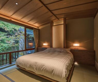 Tatami room with low bed, shoji screens and large window overlooking greenery at Nishimuraya Honkan