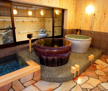 Indoor bathing area with ceramic and wooden tubs, stone floor and bamboo screen at Nissho Besso Kyoto