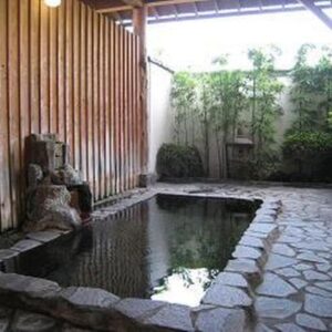 Stone-lined outdoor onsen with wooden wall, stone paving and garden plants at Nitaya ryokan in Gunma