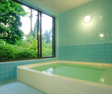 Tiled indoor soaking tub with large window and lush garden view at Nobori ryokan in Tokyo