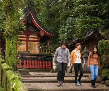 Three visitors walking past a moss-covered stone stairway and small shrine near Nogami Honkan in Ōita, Kyūshū