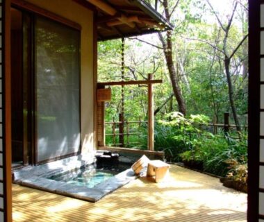 Wooden-framed soaking bath on a deck beside shoji doors overlooking a lush garden at Nonohanatei Komurasaki, Shizuoka