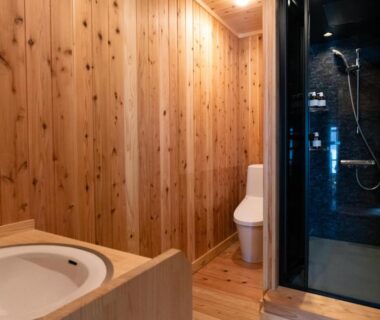 Bathroom with wooden walls, sink, toilet and glass-enclosed shower at Nunoya Ryokan in Nagano