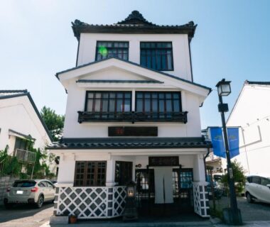 Three-story white ryokan entrance with lattice lower facade on a Nagano street