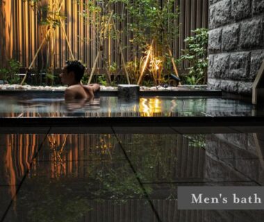 Man relaxing in indoor onsen bath with bamboo screens and stone wall at ONSEN RYOKAN Yuen Sapporo, Hokkaidō