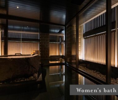 Dimly lit indoor women's onsen bath with stone tub and wooden slatted walls at ONSEN RYOKAN Yuen Sapporo Hokkaidō