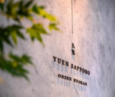 Textured concrete wall with Yuen Sapporo Onsen Ryokan signage and softly lit foliage in foreground