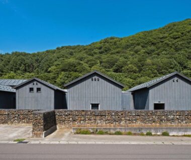 Row of gray wooden buildings and stone wall at OTARU RETREAT by Onko Chishin in Hokkaidō, Japan