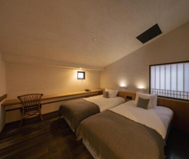 Low ceiling twin room with wooden floor and bedside lighting at OTARU RETREAT by Onko Chishin Hokkaidō