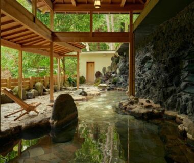 Sheltered rock-lined onsen bath with wooden deck and garden greenery at Ochiairo, Shizuoka